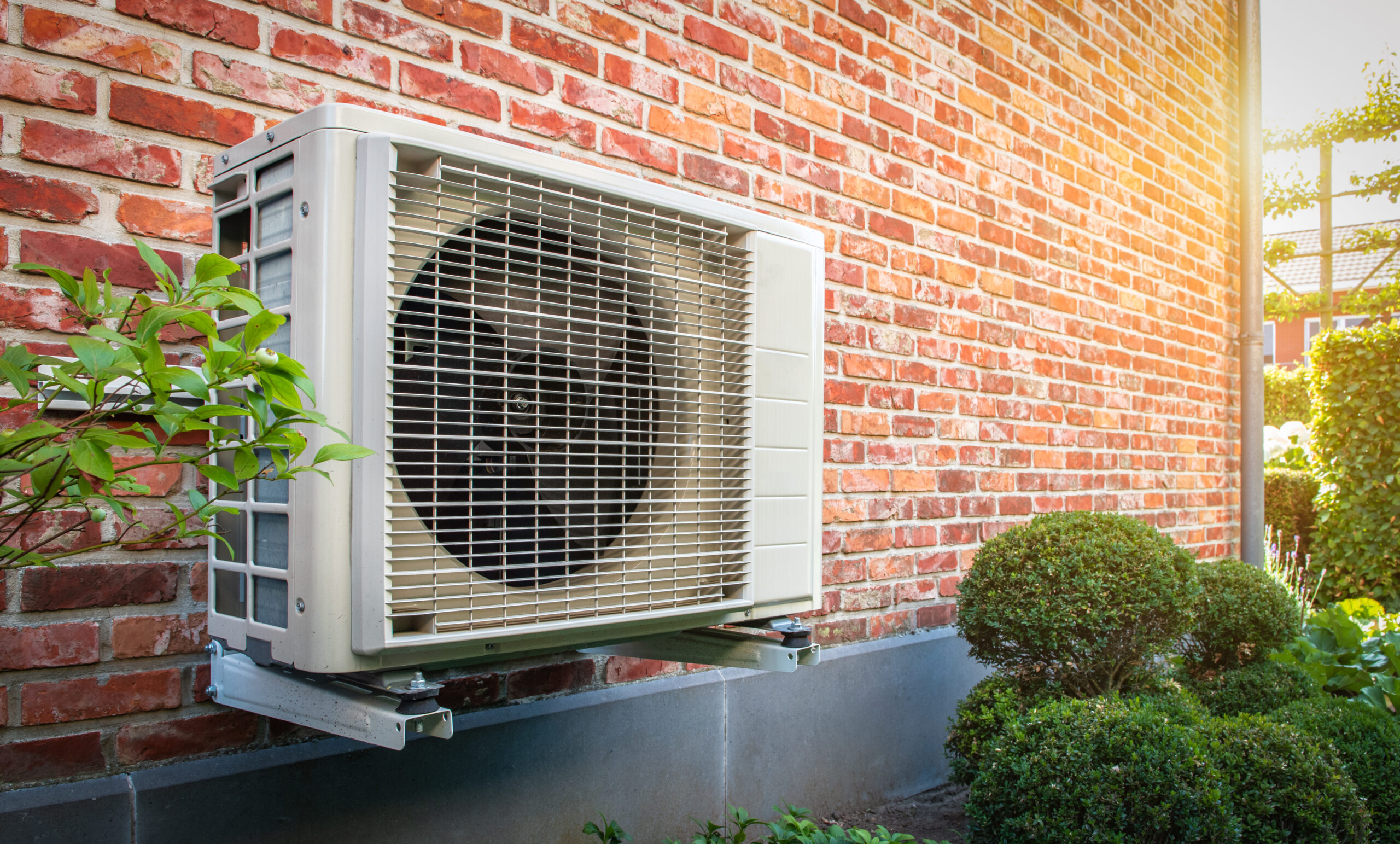 Wall-mounted heat pump against the exterior brick wall of a house.